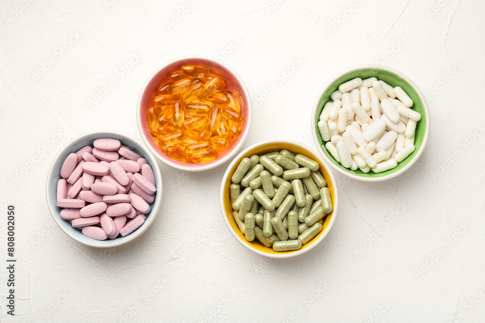 Different vitamin capsules in bowls on white wooden table, flat lay Different vitamin capsules in bowls on white wooden table, flat lay