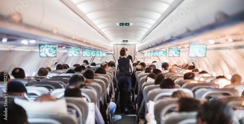 Tableau sur toile Interior of airplane with passengers on seats and stewardess in uniform walking the aisle, serving people