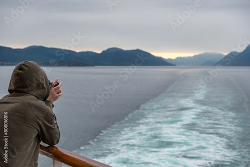 Joven tomando fotografías desde la popa de un barco que navega por los fiordos noruegos