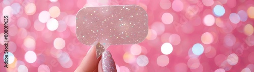 A hand with glittery nail polish holding a starshaped speech bubble against a sparkling pink background, perfect for magical messages photo