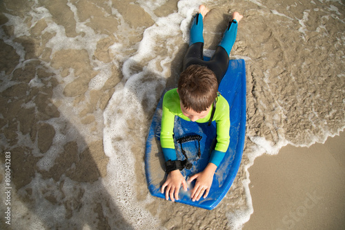 Top down view of boy wearing wetsuit riding boogie board onto the sand photo