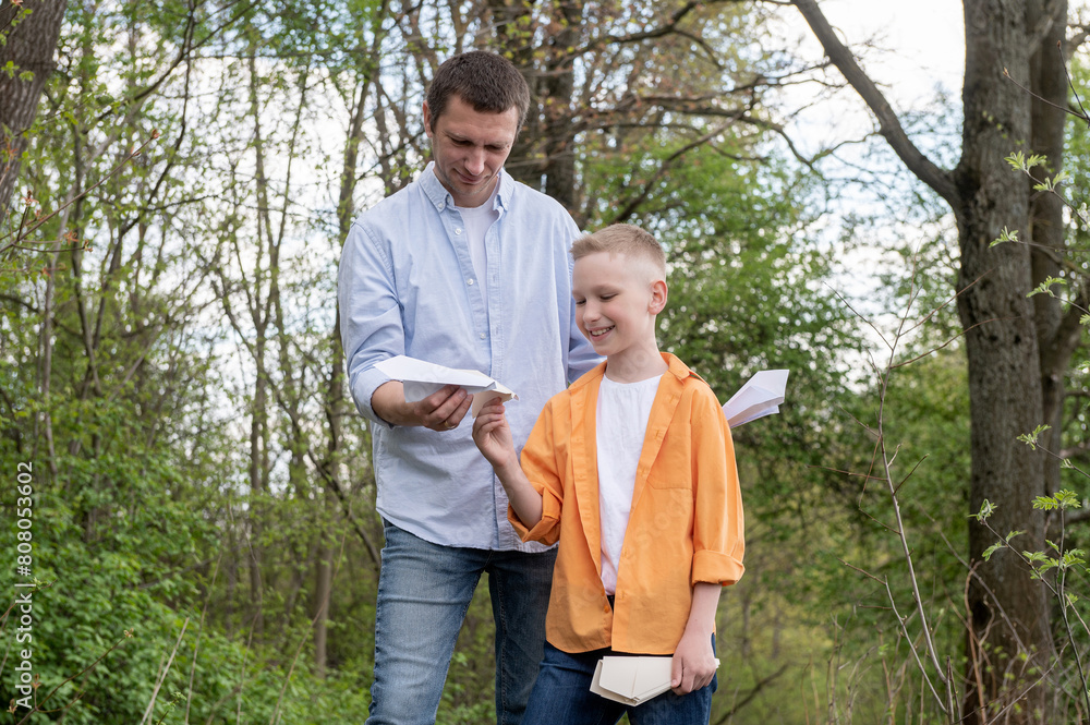 Dad showing paper plane to happy son outdoors, spending time together in nature Dad showing paper plane to happy son outdoors, spending time together in nature
