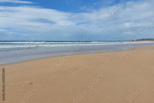 Deserted sandy beach with waves and cloudy sky. Tranquil seascape photography.