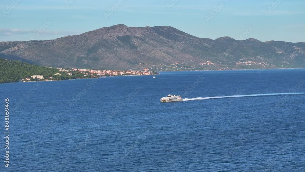 AERIAL: Large catamaran sails the deep blue Adriatic sea near the stunning Korcula island. Drone view of a public transport catamaran sailing in the Mediterranean on a sunny summer day in Croatia. AERIAL: Large catamaran sails the deep blue Adriatic sea near the stunning Korcula island. Drone view of a public transport catamaran sailing in the Mediterranean on a sunny summer day in Croatia.