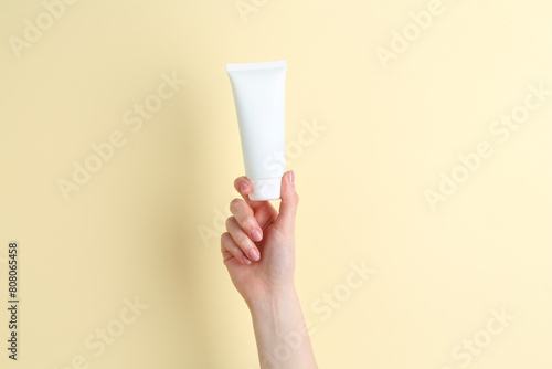 Woman holding tube of cream on yellow background, closeup