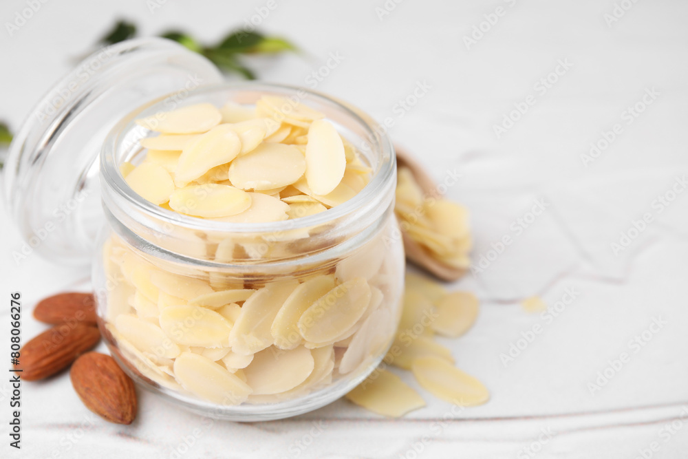 Fresh almond flakes in jar and nuts on white textured table, closeup. Space for text Fresh almond flakes in jar and nuts on white textured table, closeup. Space for text