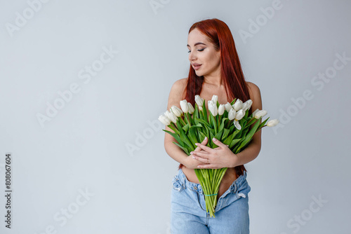 Red-haired girl in jeans with white tulips posing on a white background