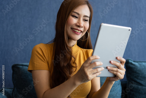 Portrait of Young attractive asian woman resting on sofa and using and looking at tablet pc in modern room communication and lifestyle concept. reading digital gadget at house.