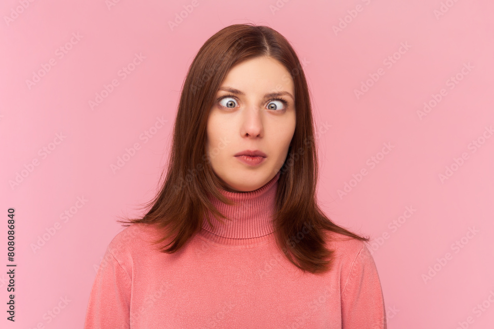 Attractive funny silly woman with brown hair with cross eyed, has stupid dumb face, awkward confused comical expression, wearing rose turtleneck. Indoor studio shot isolated on pink background Attractive funny silly woman with brown hair with cross eyed, has stupid dumb face, awkward confused comical expression, wearing rose turtleneck. Indoor studio shot isolated on pink background