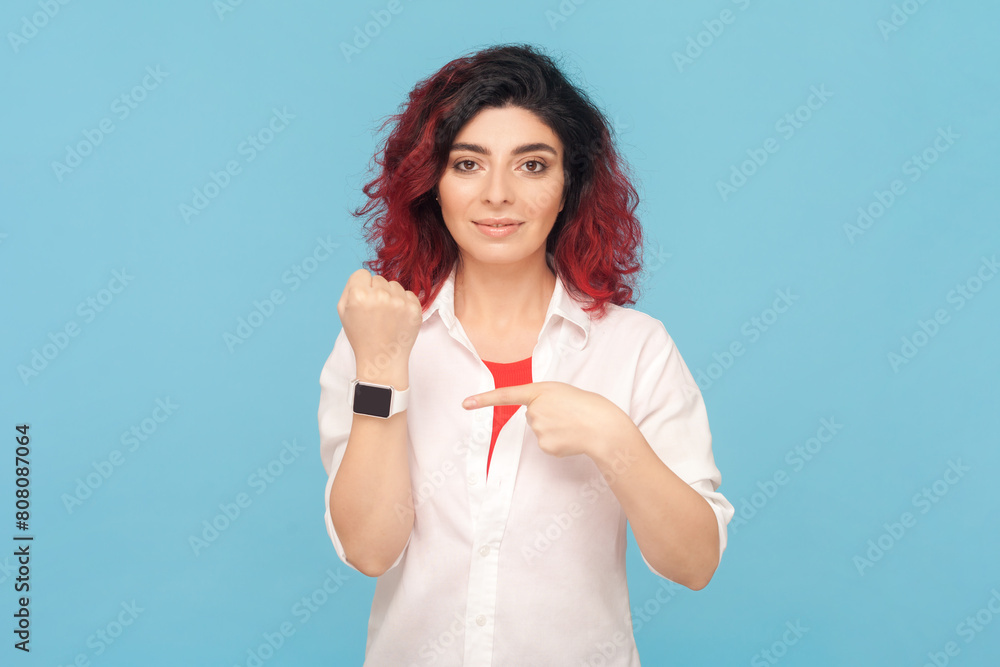 Φωτογραφία Portrait of serious attractive woman with fancy red hair standing pointing at wrist watch, reminding about deadline, wearing white shirt