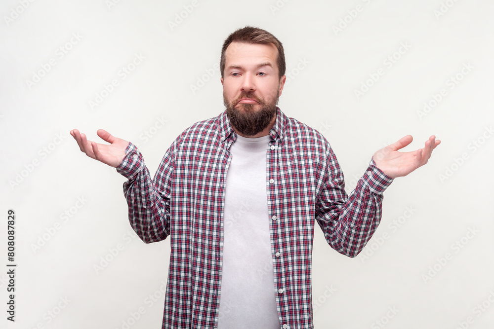 Portrait of confused uncertain bearded man shrugging shoulders doesn't know answer, wearing casual checkered shirt. Indoor studio shot isolated on gray background. Portrait of confused uncertain bearded man shrugging shoulders doesn't know answer, wearing casual checkered shirt. Indoor studio shot isolated on gray background.