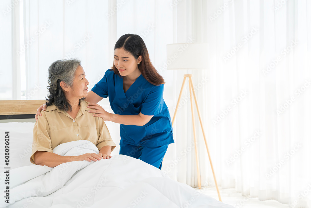 Obraz premium Doctor in blue uniform and with stethoscope hugging senior woman lying in bed at hospital.