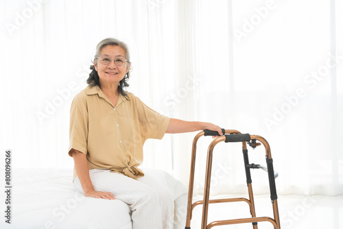 Quadro em tela A woman in a tan shirt sits on a bed with a walker next to her.