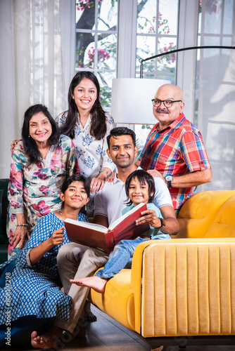 Photography Indian asian kids with parents and grand parents sitting on sofa and watching ph