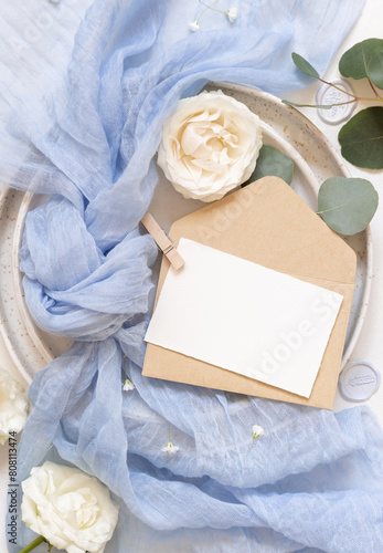 Card and envelope near blue tulle fabric and cream roses top view copy space, wedding mockup