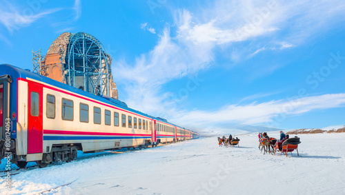 Red diesel train (East express) in motion at the snow covered railway - Horses pulling sleigh in winter - Ani Ruins, Ani is a ruined and  medieval Armenian city - Kars, Turkey photo