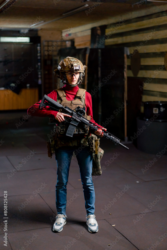 Naklejka premium at a professional shooting range girl in tactical ammunition stands with a NATO rifle