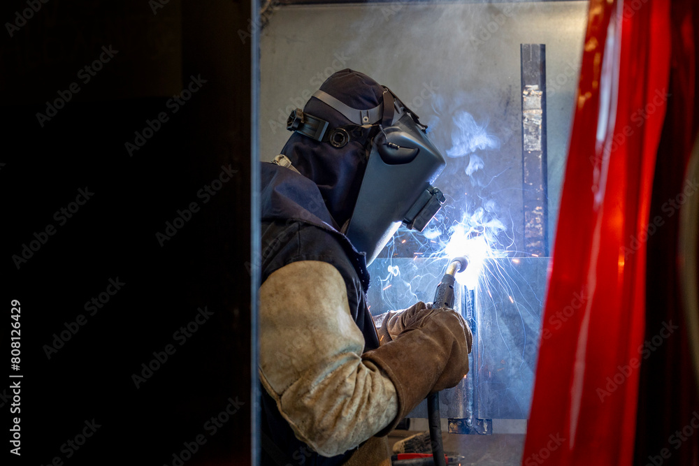 A skilled welder in protective gear works attentively with metal, creating intense sparks while welding in a dark setting The image captures the precision and intensity of this craftsmanship
