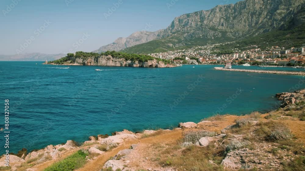 Vibrant Seascape with Lush Cliffside and Urban Backdrop. Aerial view reveals serene sea, and the bustling cityscape of Makarska town in Croatia. Vibrant Seascape with Lush Cliffside and Urban Backdrop. Aerial view reveals serene sea, and the bustling cityscape of Makarska town in Croatia.
