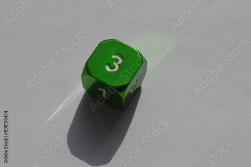 Green D6 die showing 3 in sunlight on white background