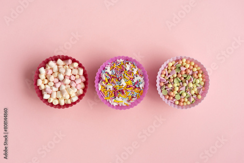 Set of colorful sprinkles and marshmallows to decorate Easter cupcake, cake, cookies or ice cream on pink background. Top view