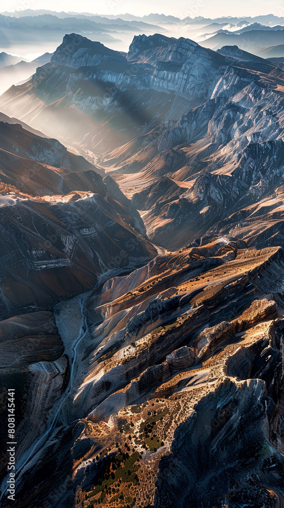 An expansive panorama showing the delicate interplay of light and shadow across a mountain wilderness at sunrise, 