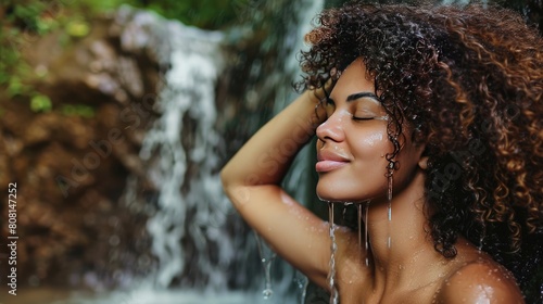 Woman rinsing her curly hair under a natural waterfall, emphasizing the cleanliness and natural setting.