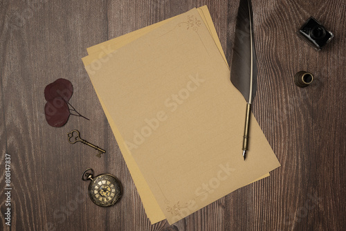 Vintage quill pen and empty old blank paper sheet with old accessories on wooden background from above. Flat lay, top view. Copy space