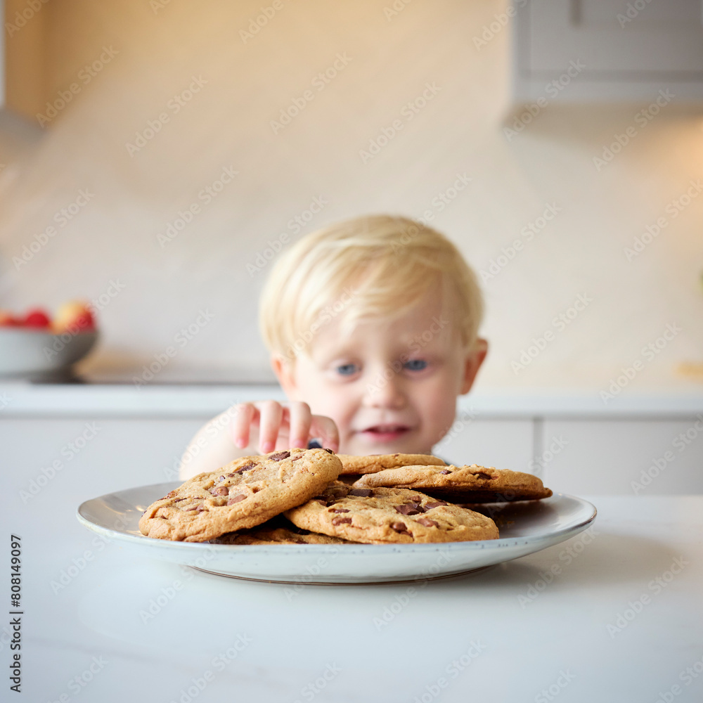 Mischievous Young Boy Taking Giant Cookie From Plate In Kitchen At Home Mischievous Young Boy Taking Giant Cookie From Plate In Kitchen At Home