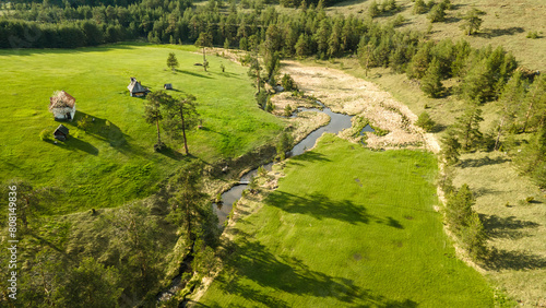 Small narrow winding river, green fields and forest aerial view. Green beautiful rural drone landscape in sunset light. Nature, sustainable and ecology concept. Crni Rzav river, Zlatibor, Serbia.