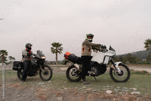 Friends motorcyclists traveling on adventure motorcycles on  seashore against backdrop of palm trees