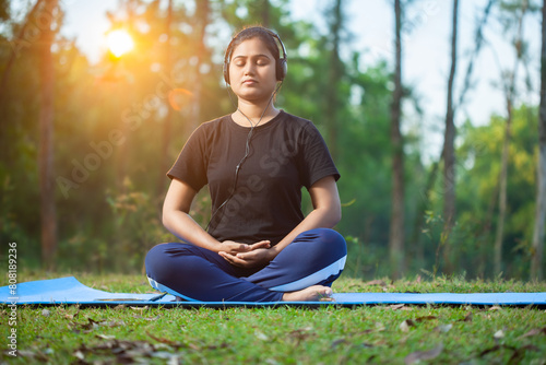 yoga women sitting in a easy pose practicing Bhairava mudra while using headphone at park in the early morning photo