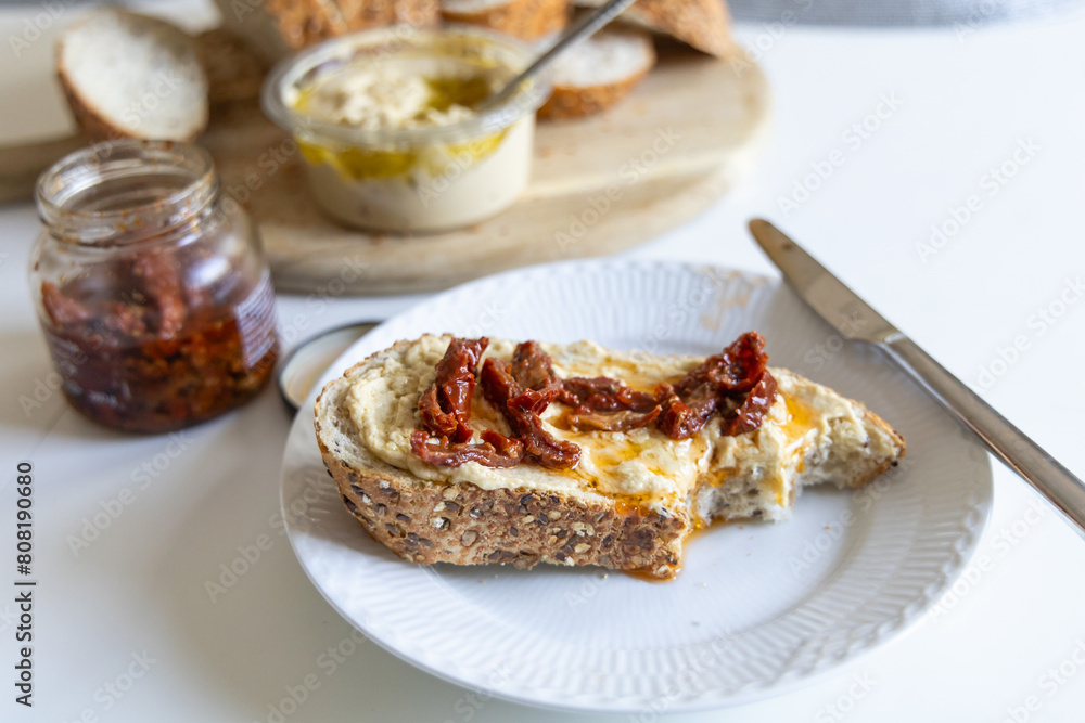 Piece of bread with hummus and sun-dried tomatoes on a white plate Piece of bread with hummus and sun-dried tomatoes on a white plate