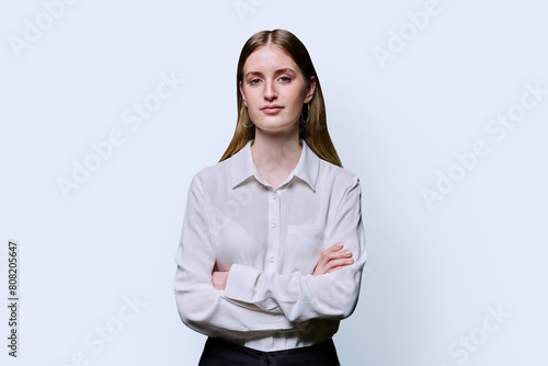 Portrait of teenage serious female in white shirt with crossed arms on studio background