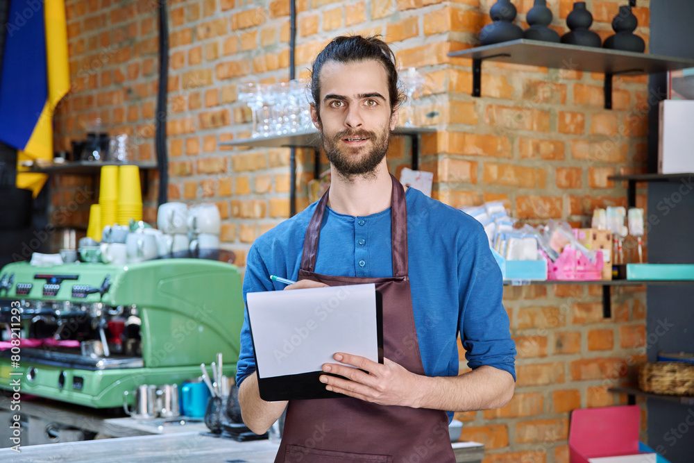 Young man in apron, food service worker, small business owner entrepreneur with work papers