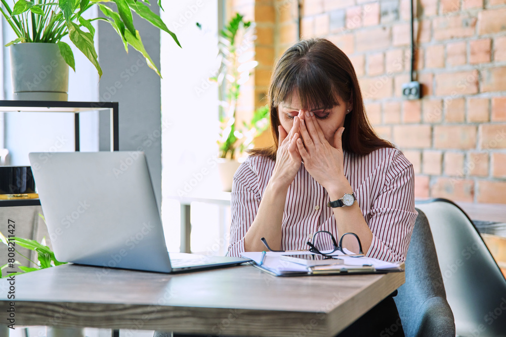 Mature tired worried tense woman at workplace experiencing stress headache Mature tired worried tense woman at workplace experiencing stress headache