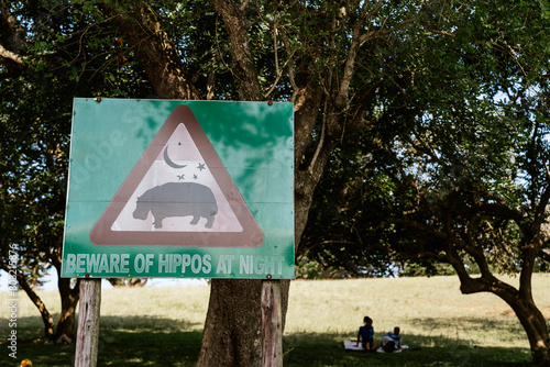 Cautionary sign warning of hippos at night with people in background photo