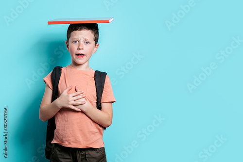 Worried schoolboy with book on head against blue background photo