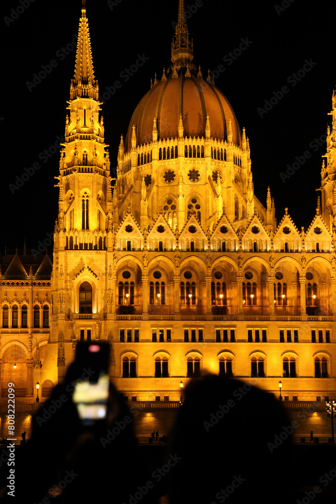 A tourist tries to capture with his phone the night view of the illuminated Hungarian Parliament building, in Budapest.