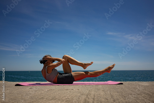 Brunette Woman Performing Isometric Exercises on Pink Exercise Mat by the Sea photo