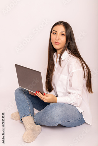 A young woman in white shirt with a laptop sits on white background.Work online
