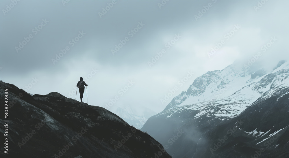 A man stands confidently on top of a mountain peak, overlooking the vast landscape below.