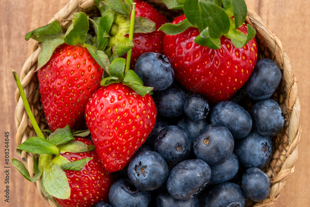 Closeup top view of blueberries and strawberries in wicker bowl on wooden table Closeup top view of blueberries and strawberries in wicker bowl on wooden table