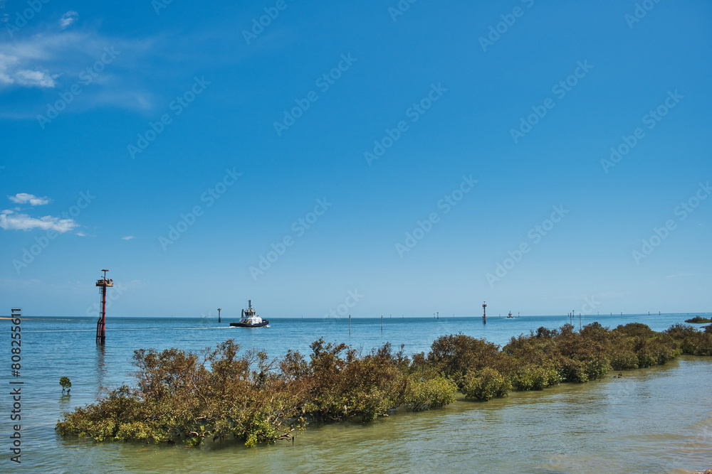 Entrance to the harbor of Port Hedland, Western Australia, with buoys, tugboat and mangrove-covered breakwater