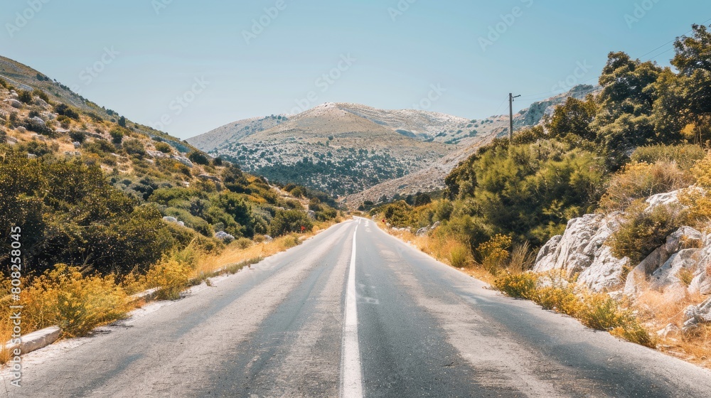 an asphalt road winding through mountainous terrain, flanked by white rocks and lush vegetation under the radiant sun.