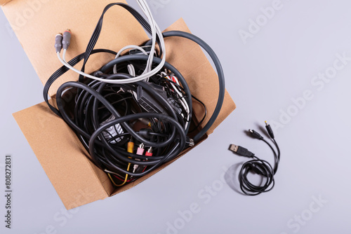 Cardboard box filled with old cables, wires, and button mobile phones against a gray background, highlighting the importance of recycling electronic waste