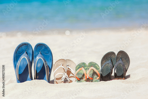 A Slippers of the whole family in the sand by the sea on nature while traveling. Rest by the water on vacation with shoes.