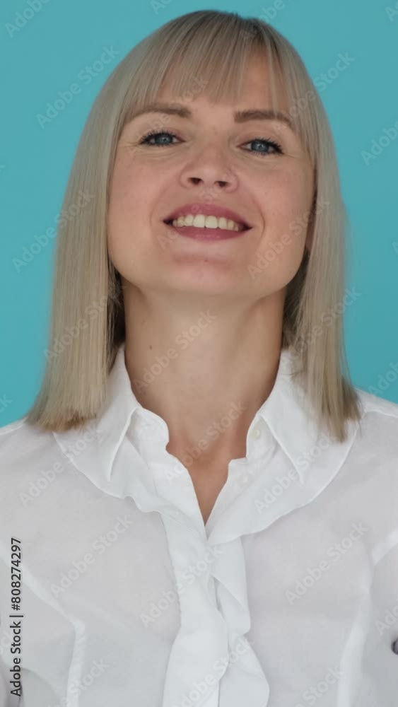 Portrait of a playful Caucasian woman showing hush gesture with finger on lips for keeping secret or privacy on blue background. Vertical video. Portrait of a playful Caucasian woman showing hush gesture with finger on lips for keeping secret or privacy on blue background. Vertical video.