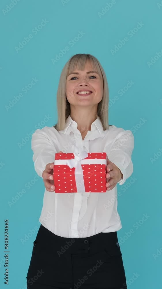 Cheerful and smiling Caucasian woman presenting gift box on blue background. Celebration, congratulation and greeting concept. Vertical video. Cheerful and smiling Caucasian woman presenting gift box on blue background. Celebration, congratulation and greeting concept. Vertical video.