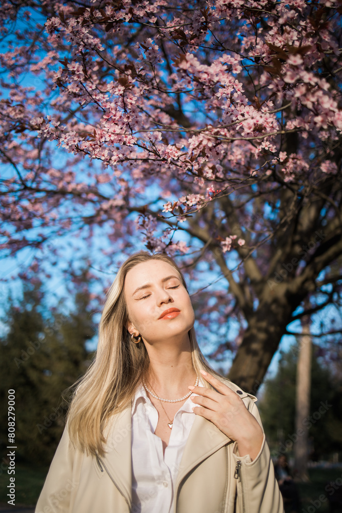 Fashion outdoor photo of beautiful woman with blond hair in elegant suit posing in spring flowering park with blooming cherry tree. Copy space and empty place for advertising text Fashion outdoor photo of beautiful woman with blond hair in elegant suit posing in spring flowering park with blooming cherry tree. Copy space and empty place for advertising text